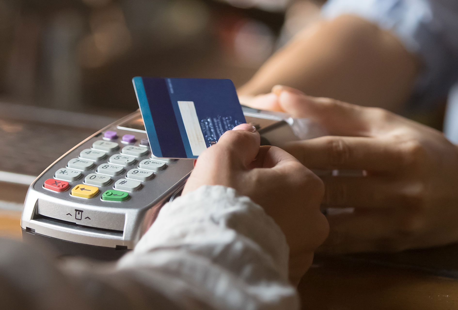 An image of two individuals' hands exchanging a Dow Credit Union contactless card over a point-of-sale terminal.